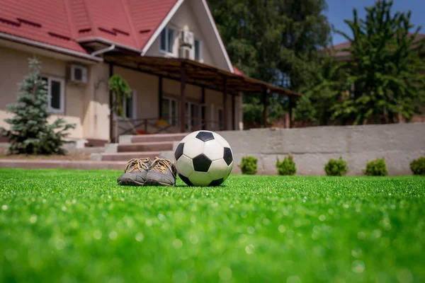 Fotboll och skor på gräsmattan mot bakgrund av hus med terrass. Hem fotboll koncept — Stockfoto