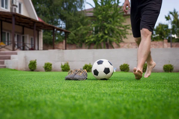 Ноги футболиста тренируются дома, пиная мяч без обуви на зеленой траве в саду — стоковое фото