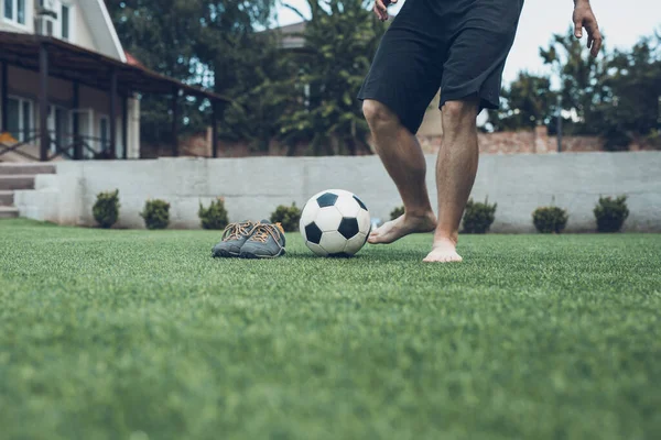 Ben av fotboll spelare utbildning hemma sparkar bollen utan skor på grönt gräs i trädgården — Stockfoto