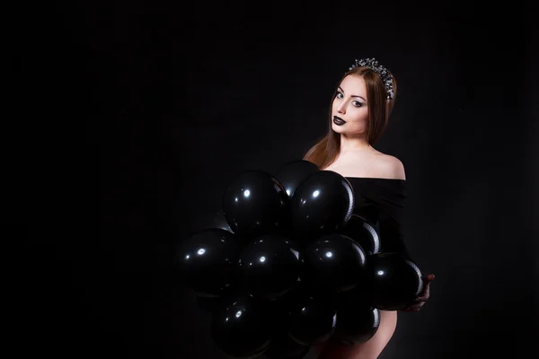 Sexy young woman with perfect body wearing black lingerie. Beautiful fashion model posing in dramatic light holding baloons — Stock fotografie