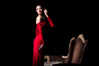  Elegant woman in red dress in darkness. Female in dramatic light