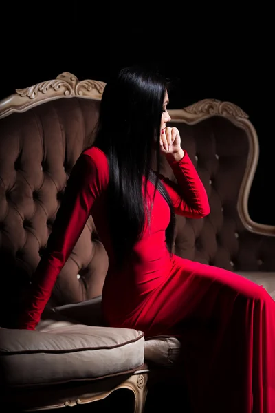 Mooie dame in rode jurk op luxe sofa — Stockfoto