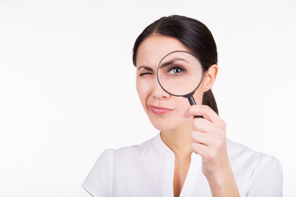 Красивая девушка ищет с увеличителем. Белый фон
