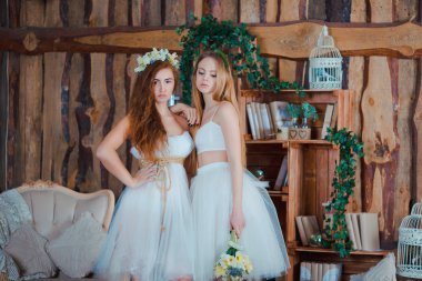 Two beautiful sensual brides standing in vintage interior holding flowers
