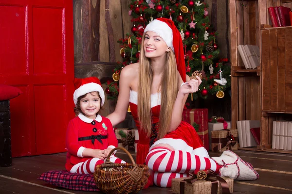 Due ragazze che indossano il vestito di Natale e cappello che decorano l'albero di Natale. Anno nuovo interno . — Foto Stock