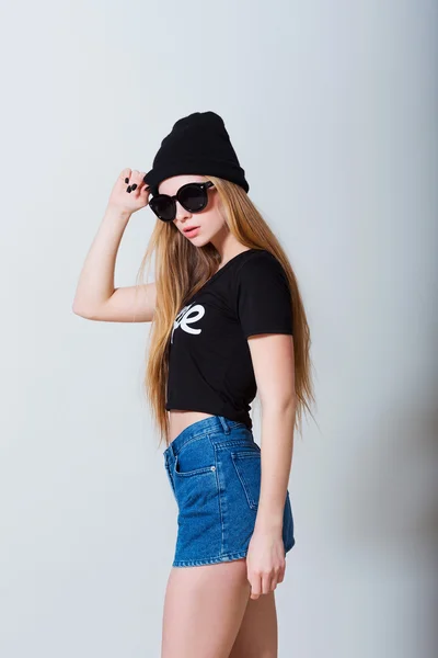 Fashion portrait of beautiful sexy young girl in jeans shorts and sun glasses on white background — Stock Photo, Image