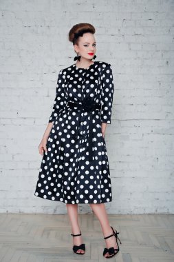 Beautiful sexy young female in fashion clothes posing next to white brick wall.