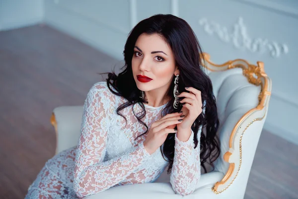 Ritratto perfetto di giovane donna sexy con labbra rosse che indossa seducente abito bianco seduto su una sedia vintage di lusso — Foto Stock