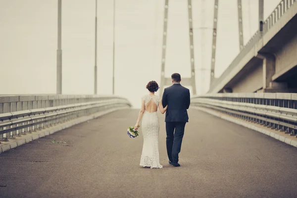 Feliz novia y novio celebrando el día de la boda. Pareja casada marchándose en el puente. Larga vida familiar concepto de carretera. Imagen tonificada —  Fotos de Stock