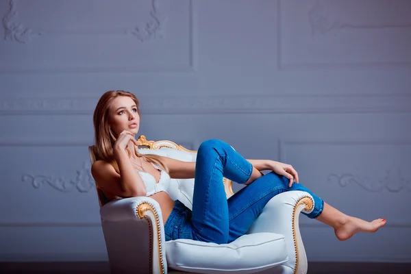 Sexy bela jovem posando na cadeira vintage. Menina em jeans e sutiã branco . — Fotografia de Stock