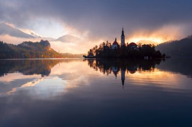Julian Alpleri 'ndeki Triglav Ulusal Parkı' nda bulunan ünlü Bled Gölü, Slovenya, Avrupa 'da gündoğumunda sonbahar renklerinde bir ormanla