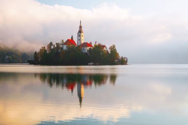 Julian Alpleri 'ndeki Triglav Ulusal Parkı' nda bulunan ünlü Bled Gölü, Slovenya, Avrupa 'da gündoğumunda sonbahar renklerinde bir ormanla