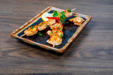 Ahşap arka planda servis edilen bir tabakta baharatlı ızgara karides.