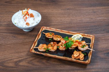 Ahşap bir arka planda servis edilen baharatlı ve pirinçli ızgara karides.