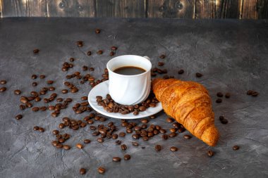Kahve çekirdekleri ve kahve fincanı, koyu ahşap arka planda taze kruvasan.