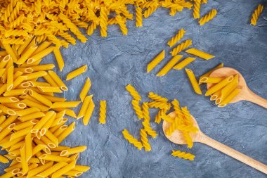 Koyu taş desenli arka planda tahta kaşıklara karıştırılmış çiğ makarna.