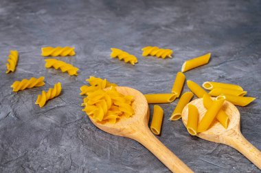 Koyu taş desenli arka planda tahta kaşıklara karıştırılmış çiğ makarna.