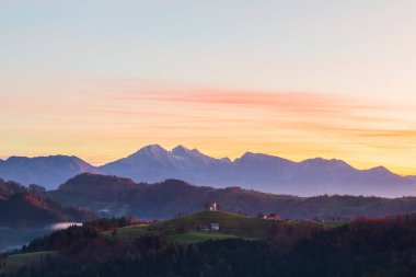 Slovenya 'nın Yukarı Carniola bölgesindeki Skofja Loka yakınlarında, sonbaharda güzel bir gündoğumunda Sveti Tomaz Kilisesi (Saint Thomas) bir tepenin üzerinde