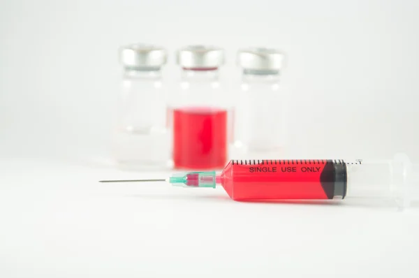 Rode vloeistof in injectie spuit en flesjes achtergrond — Stockfoto