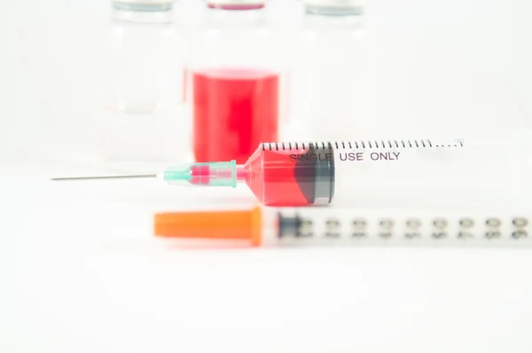 Rode vloeistof in injectie spuit en flesjes achtergrond — Stockfoto