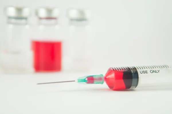 Kırmızı sıvı enjeksiyon şırınga ve şişeleri arka planda — Stok fotoğraf