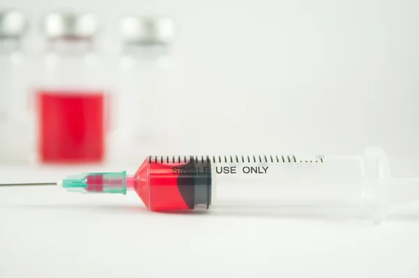 Injekciós fecskendő és fiolák háttérben vörös folyadék — Stock Fotó
