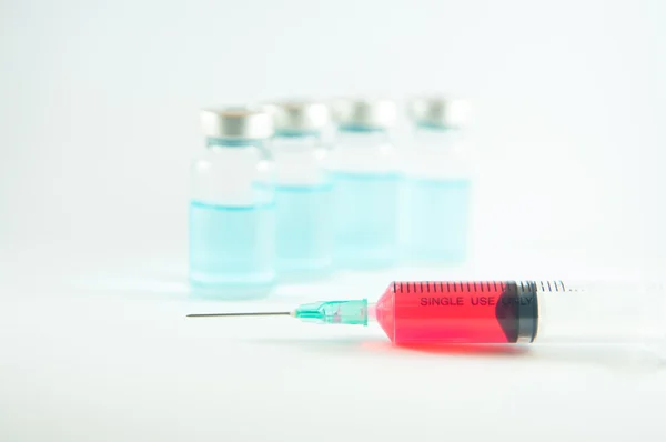 Červená kapalina v injekční stříkačky a lahvičky pozadí — Stock fotografie