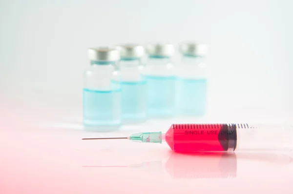 Červená kapalina v injekční stříkačky a lahvičky pozadí — Stock fotografie