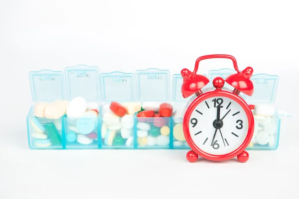 Medicine in weekly pill box and red alarm clock — Stock Photo, Image