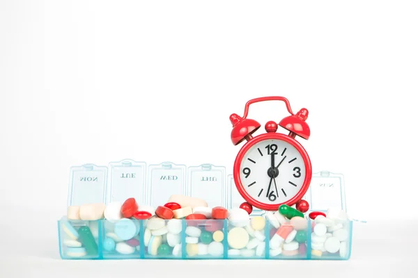 Red alarm clock and medicine in weekly pill box — Stock Photo, Image