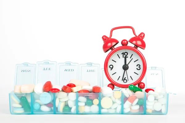 Medicine in weekly pill box and red alarm clock — Stock Photo, Image