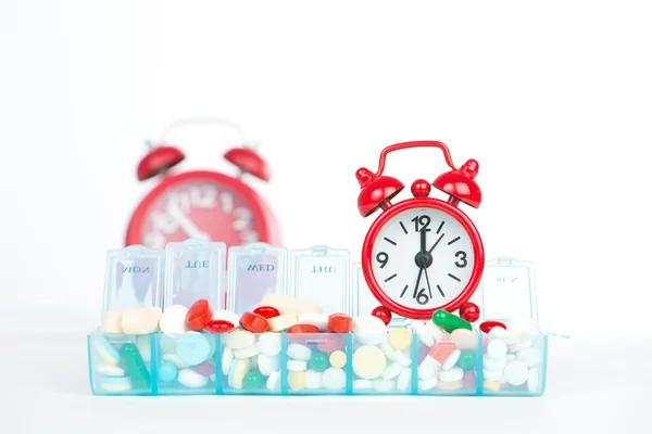 Red alarm clock and medicine in weekly pill box — Stock Photo, Image