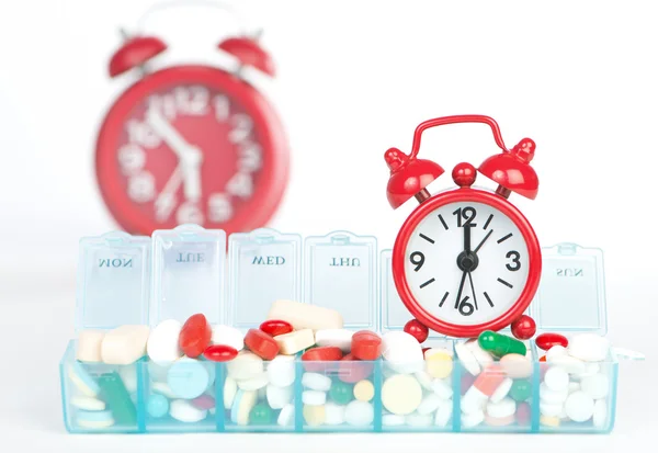 Red alarm clock and medicine in weekly pill box — Stock Photo, Image