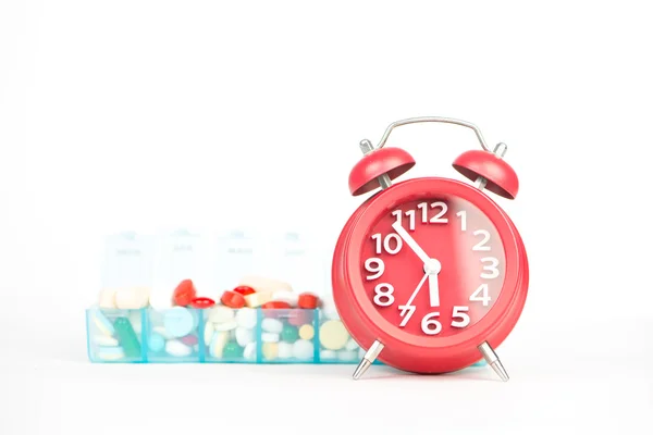 Red alarm clock and medicine in weekly pill box — Stock Photo, Image