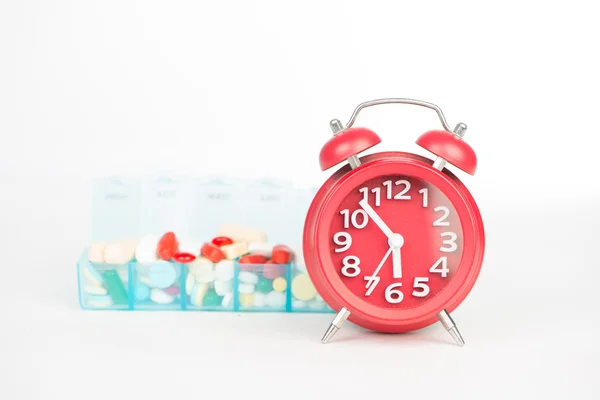Jam alarm merah dan obat-obatan dalam kotak pil mingguan — Stok Foto