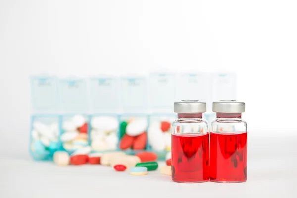 Флаконы с инъекциями и лекарства в еженедельную коробку с таблетками — стоковое фото