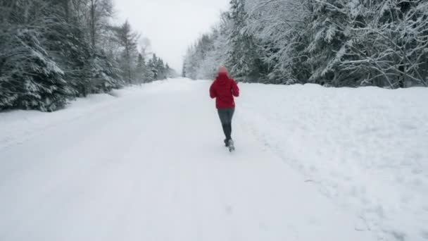Жінка біжить по засніженій віддаленій дорозі — стокове відео