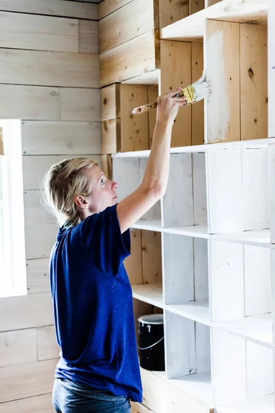 Femme appliquant la première couche de peinture sur une bibliothèque en bois — Photo
