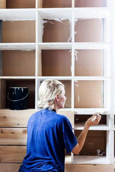 Mujer aplicando la primera capa de pintura en una biblioteca de madera — Foto de Stock