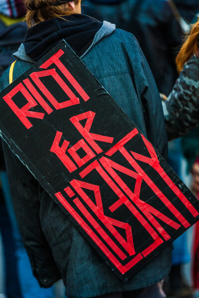  Closeup of the Back of a protester Wearing a Sign Saying "Riot 