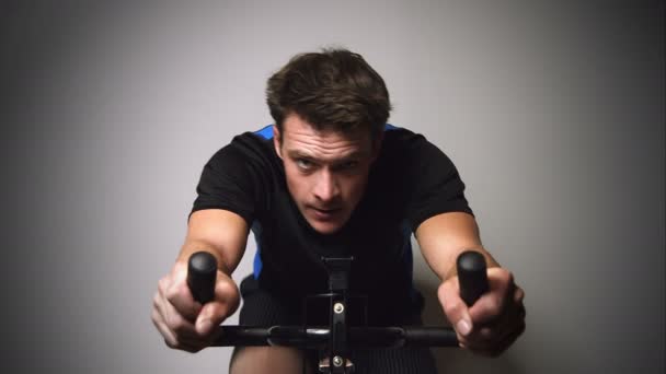 Motivierter junger Mann sprintet und schwitzt auf stationärem Fahrrad — Stockvideo