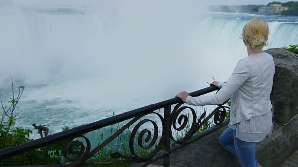 Молодая блондинка, смотрящая на Ниагарский водопад — стоковое видео