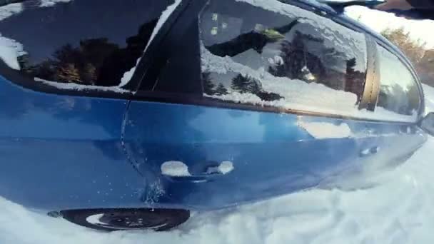 Человек убирает снег из своей синей машины — стоковое видео