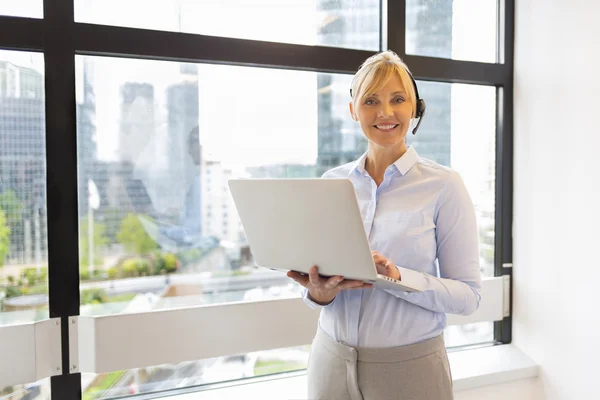 Attractive Business woman working on laptop. Headset. Building b — Stock Photo, Image