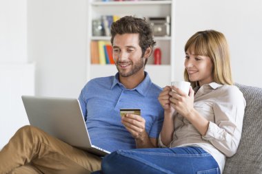 Evde laptop ve kredi kartı kullanarak alışveriş orta yetişkin çift
