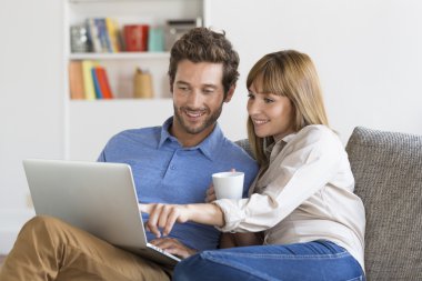 Genç çift evde kanepe üstünde laptop ile internette sörf