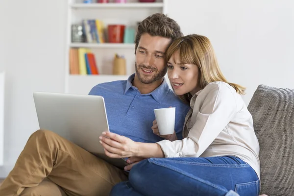 Pareja joven usando el ordenador portátil en el sofá en casa — Foto de Stock