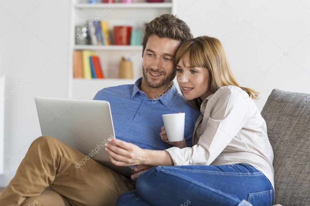 Young couple using laptop on sofa at home