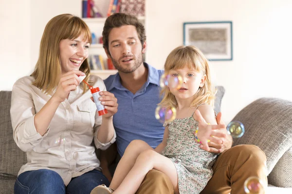 Vrolijke ouders en dochter waait bubbels in wit modern ho — Stockfoto
