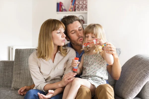 Vrolijke ouders en dochter waait bubbels in wit modern ho — Stockfoto